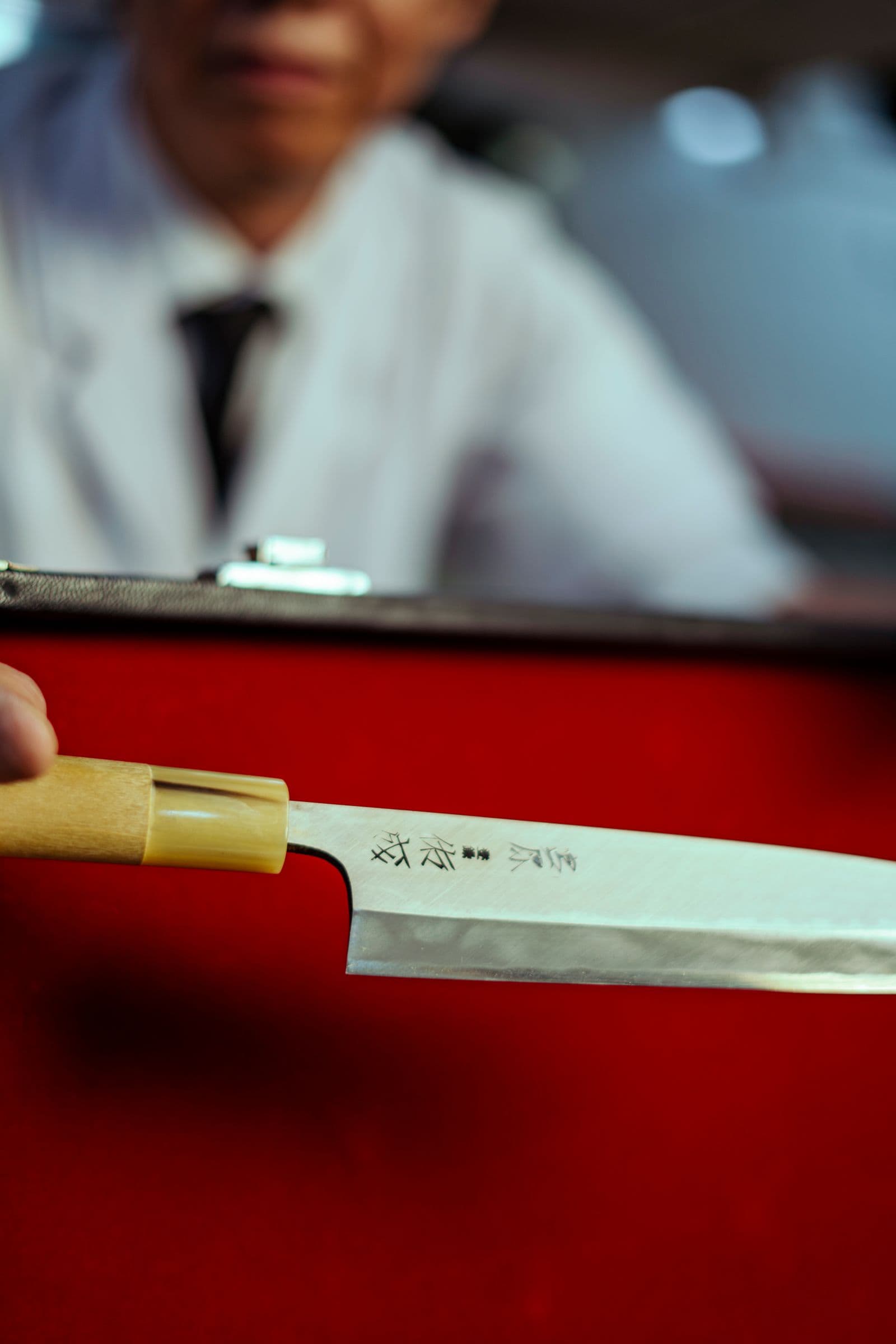 An artisan presenting a single-bevel Japanese knife with a maker's mark