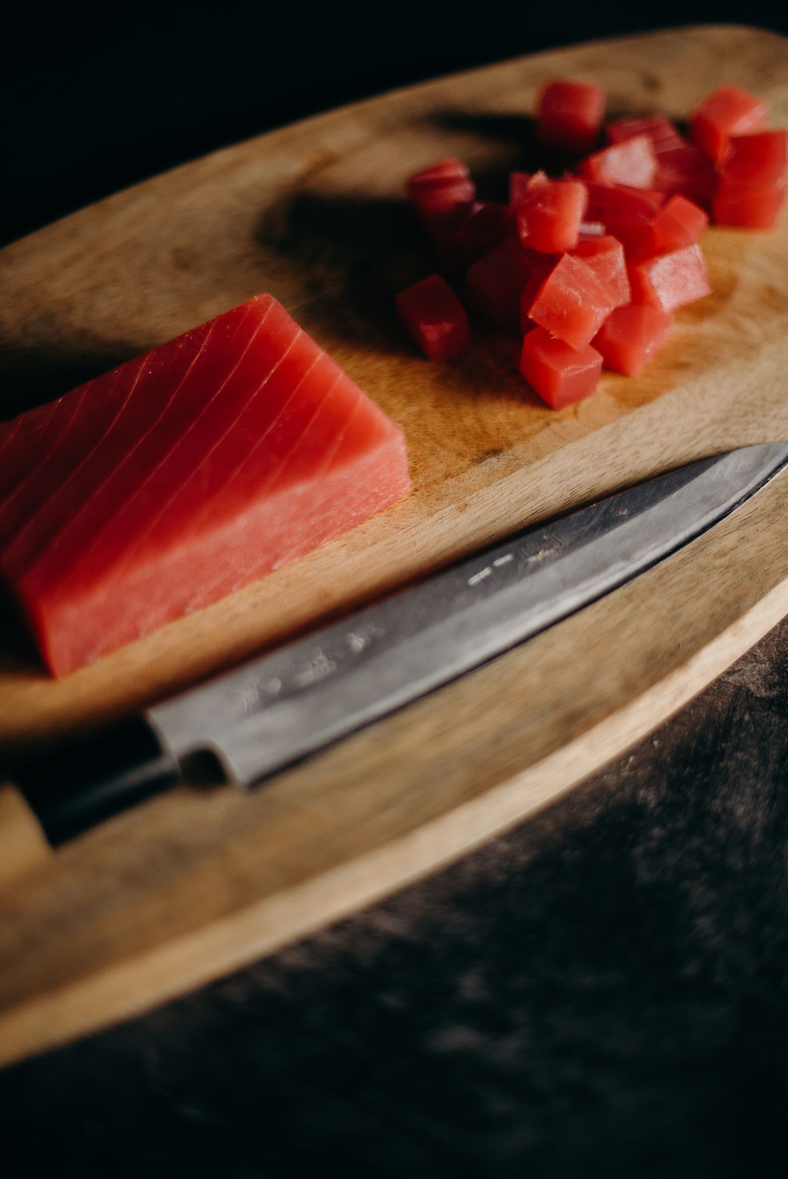 A saku block of tuna and diced tuna on a wooden board beside a Japanese knife