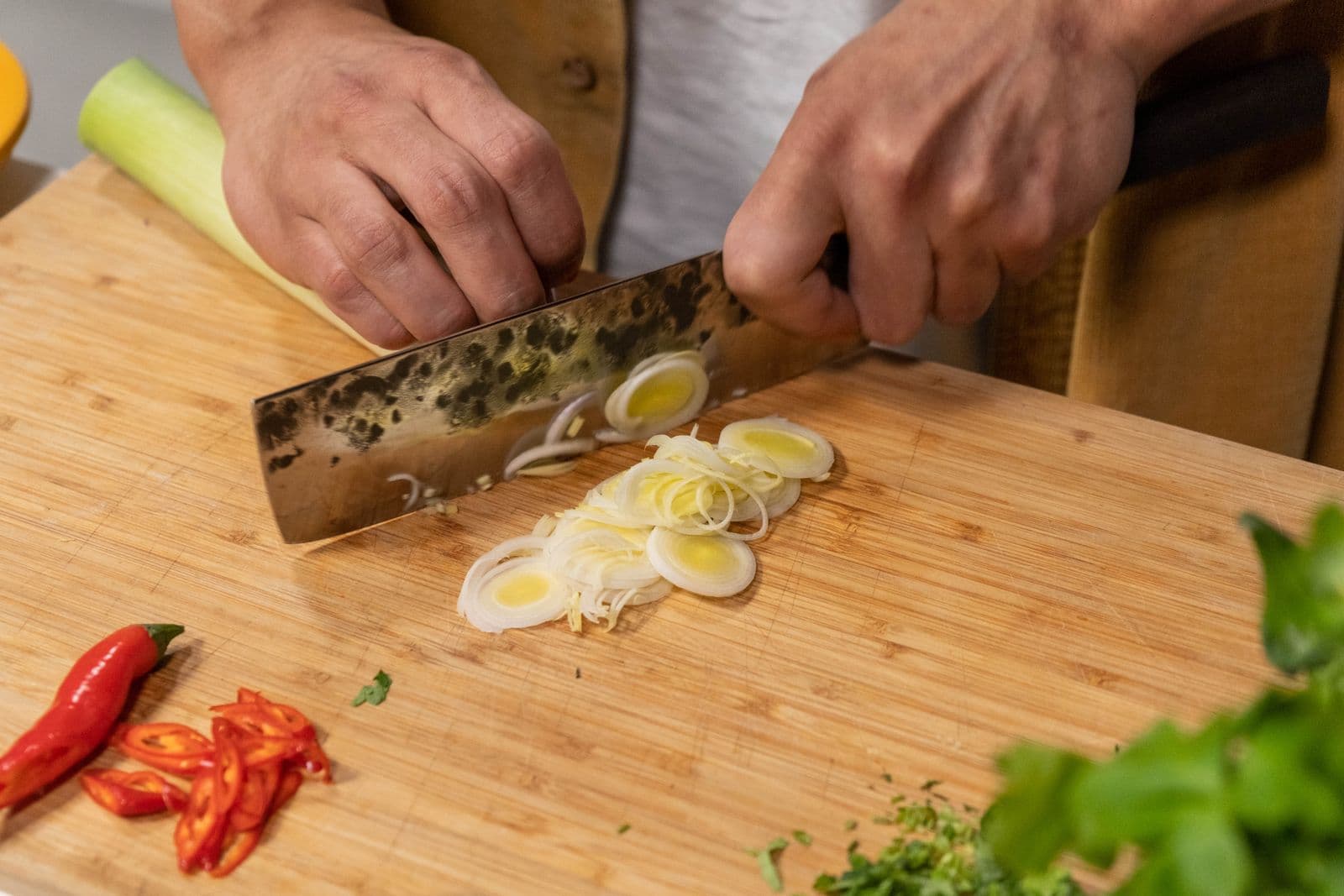 A kurouchi Japanese vegetable knife slicing leeks on a wooden board